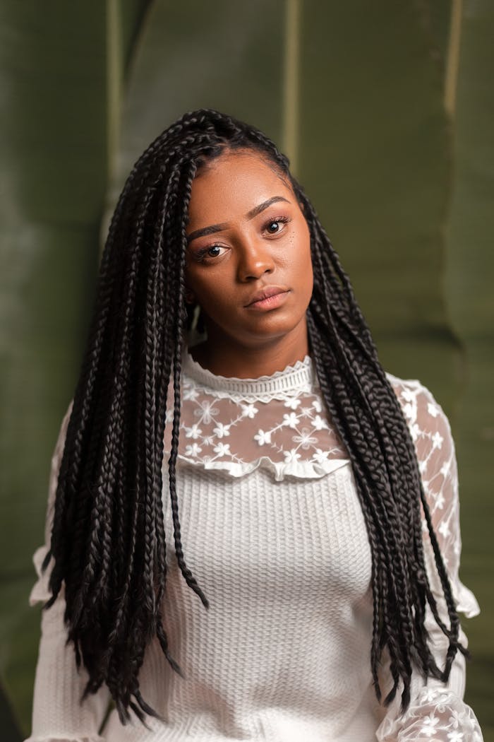 Close-up portrait of a woman with braided hair in a white top against a green backdrop.