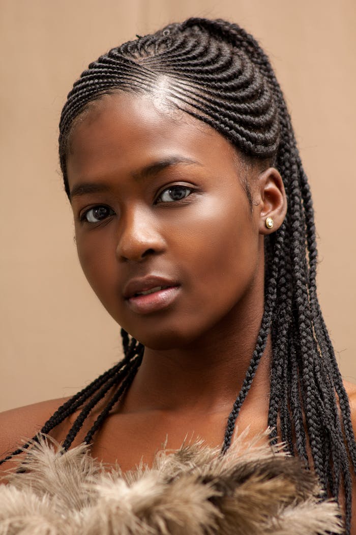 Close-up portrait of a young woman with intricate braided hairstyles in a studio setting.