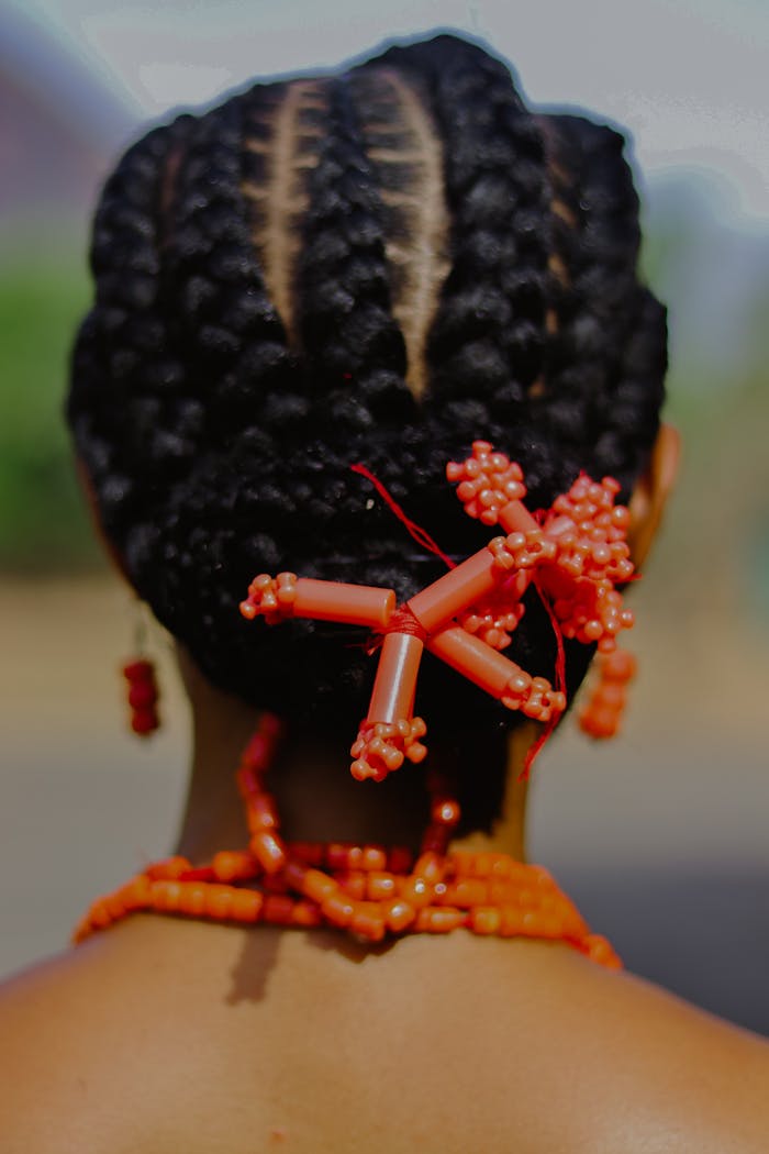 Rear view of a braided hairstyle adorned with vibrant orange beads, reflecting cultural elegance.