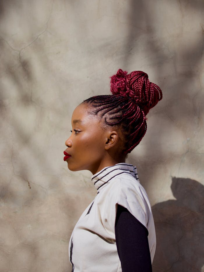 Elegant side profile portrait of a woman with intricate braided hair against a textured wall.