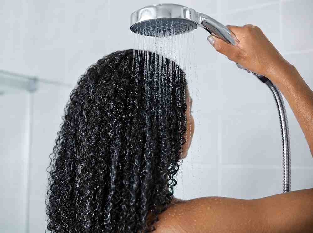 shower head with cool water running over natural curly hair to close the hair cuticle after washing